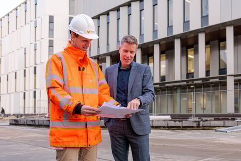 Twee collega's nemen de plannen op de bouwplaats door