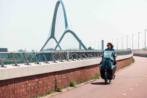 Vrouw op bakfiets fietst over een brug.