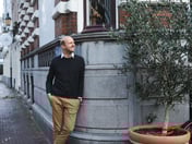 Man leunt tegen een stenen muurtje aan en kijkt lachend naar rechts.