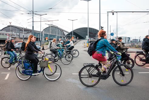 Een grote groep mensen fietst langs het centraal station in Amsterdam.
