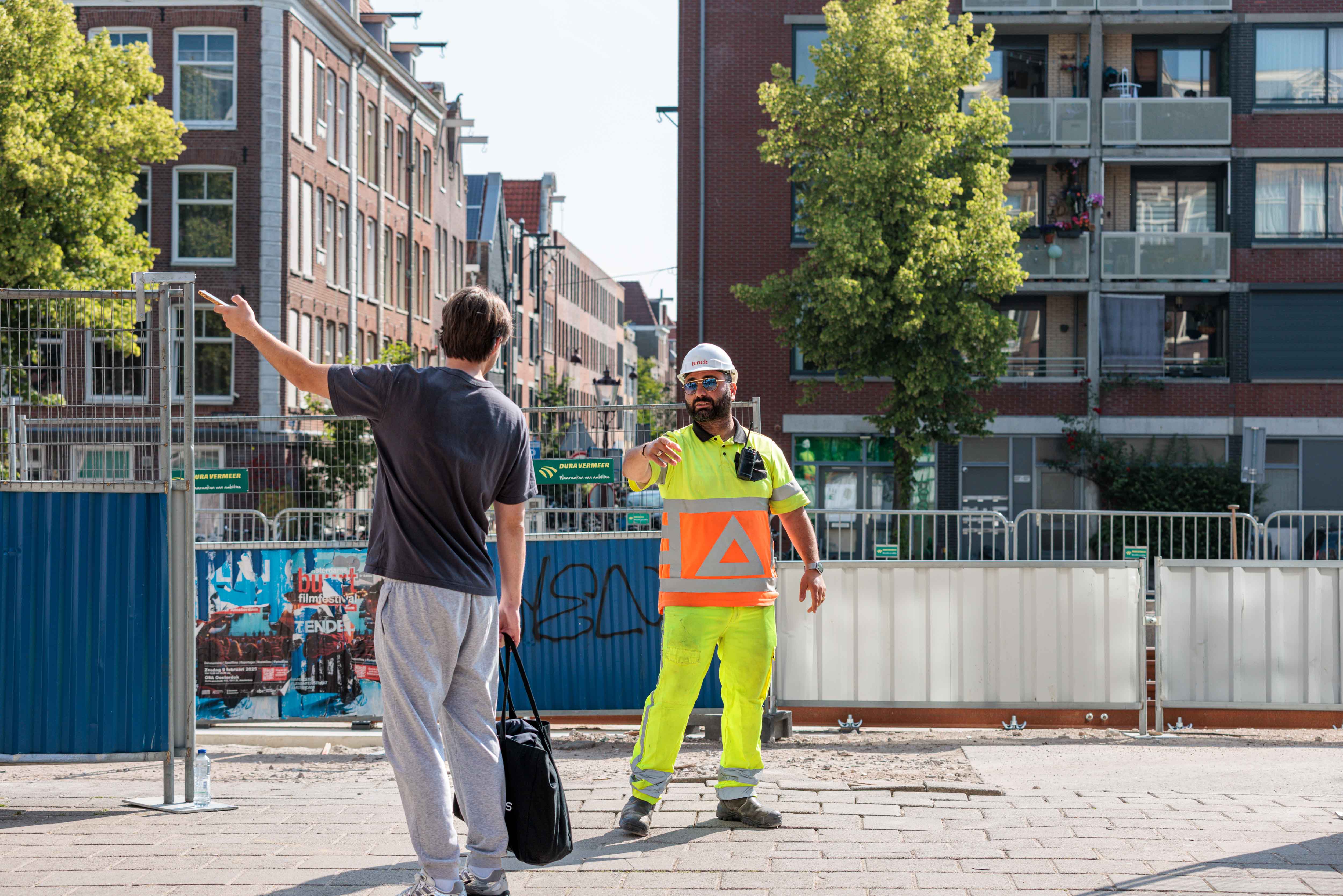 Een jongen wijst naar links en spreekt met een verkeersleider op straat.