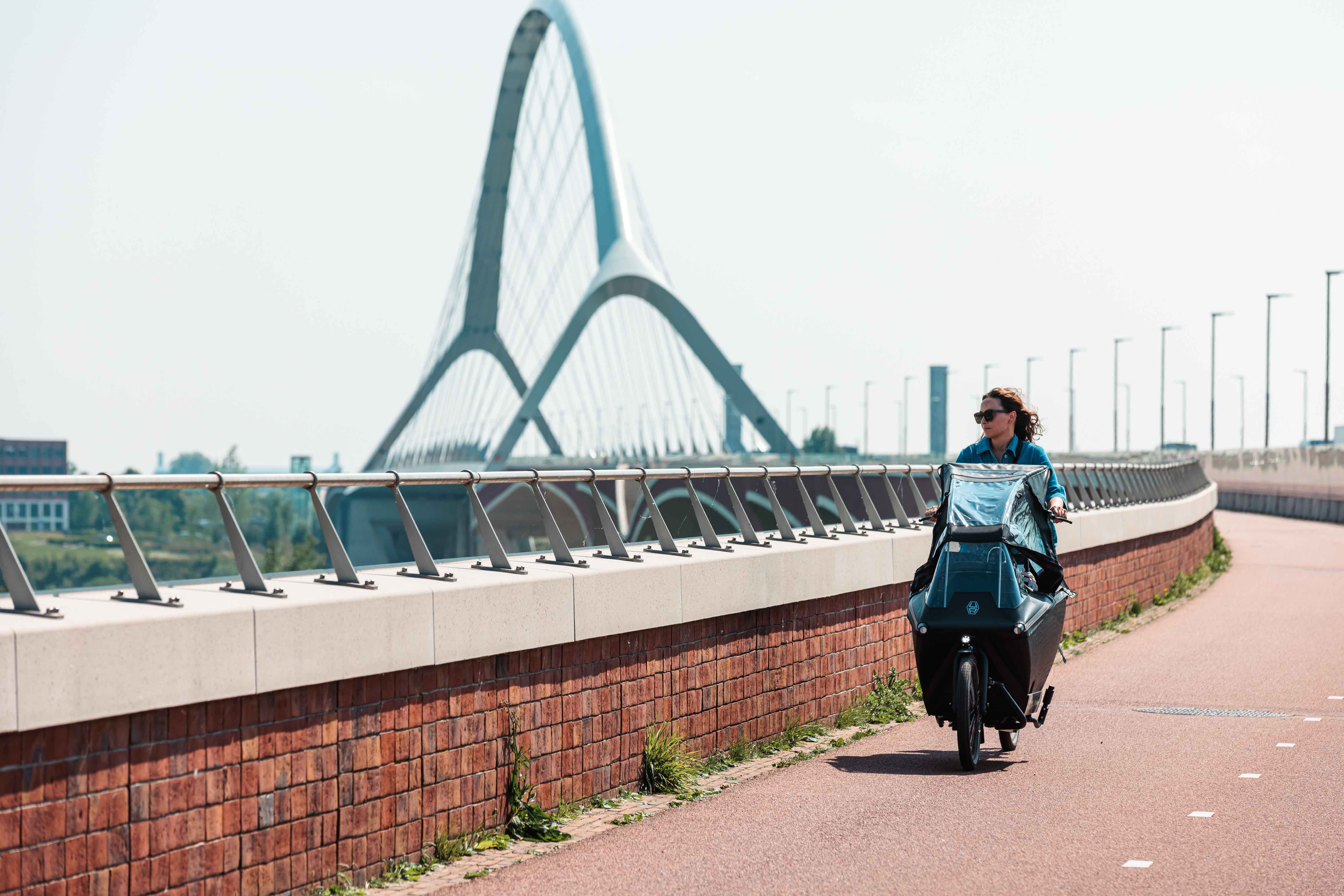 Vrouw op bakfiets fietst over een brug.