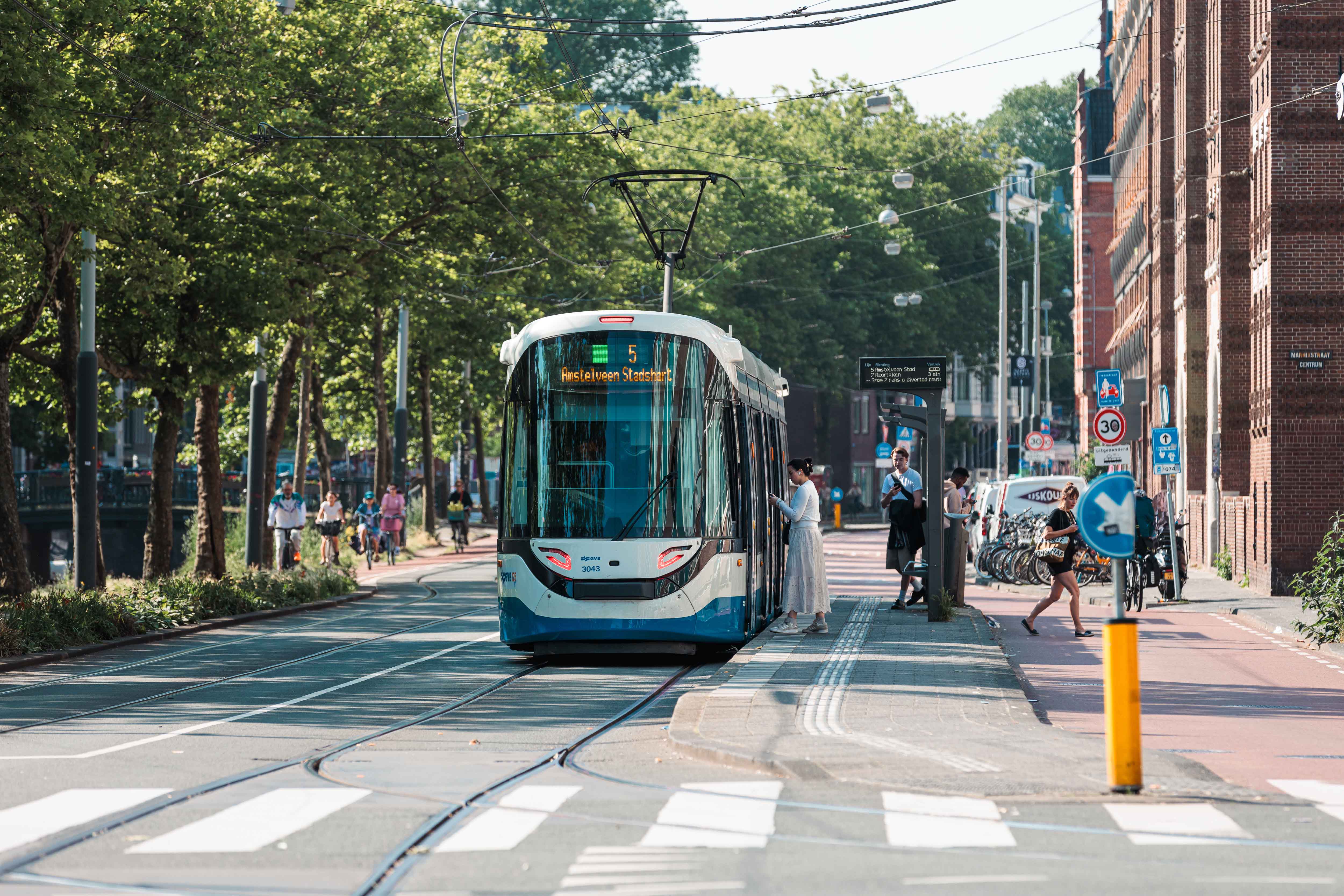 Een tram staat stil bij de tramhalte en een jonge vrouw stapt in.