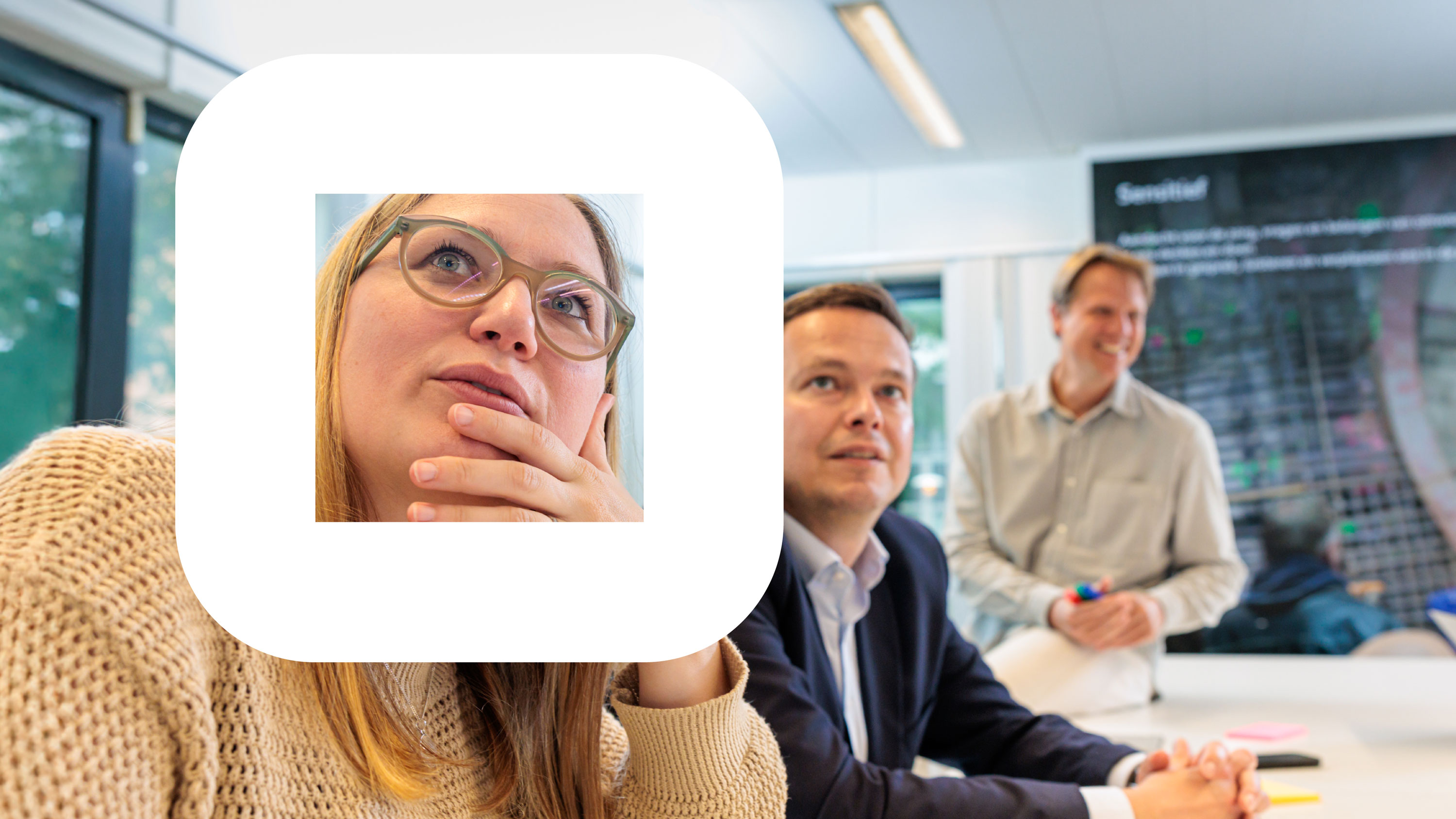 Drie mensen in een vergaderruimte, met een vrouw op de voorgrond die nadenkend kijkt.