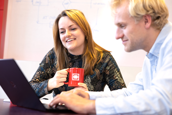 vrouwelijke-collega-kijkt-vrolijk-mee-op-laptop-mannelijke-collega