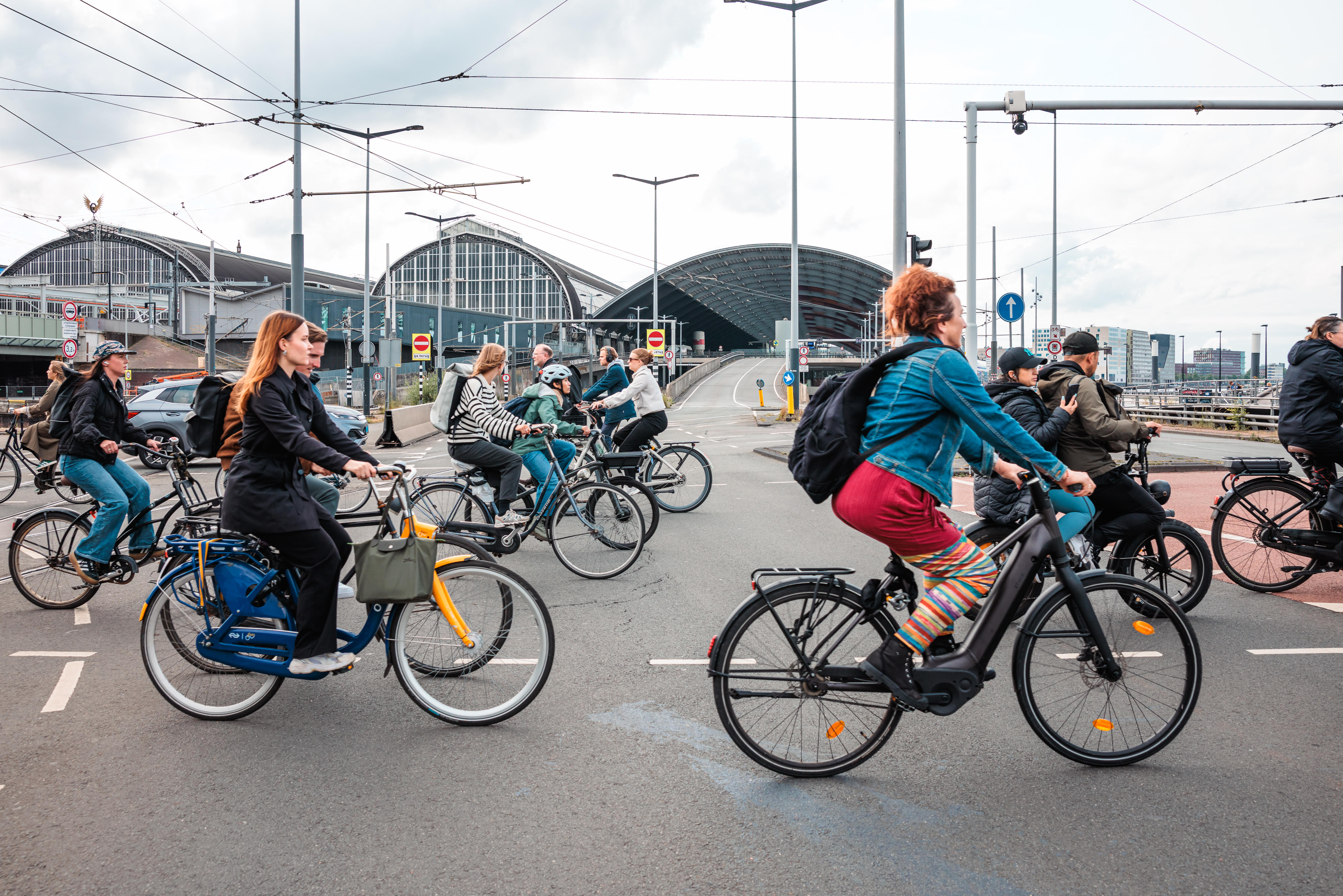 een grote groep mensen fietst langs het centraal station in amsterdam